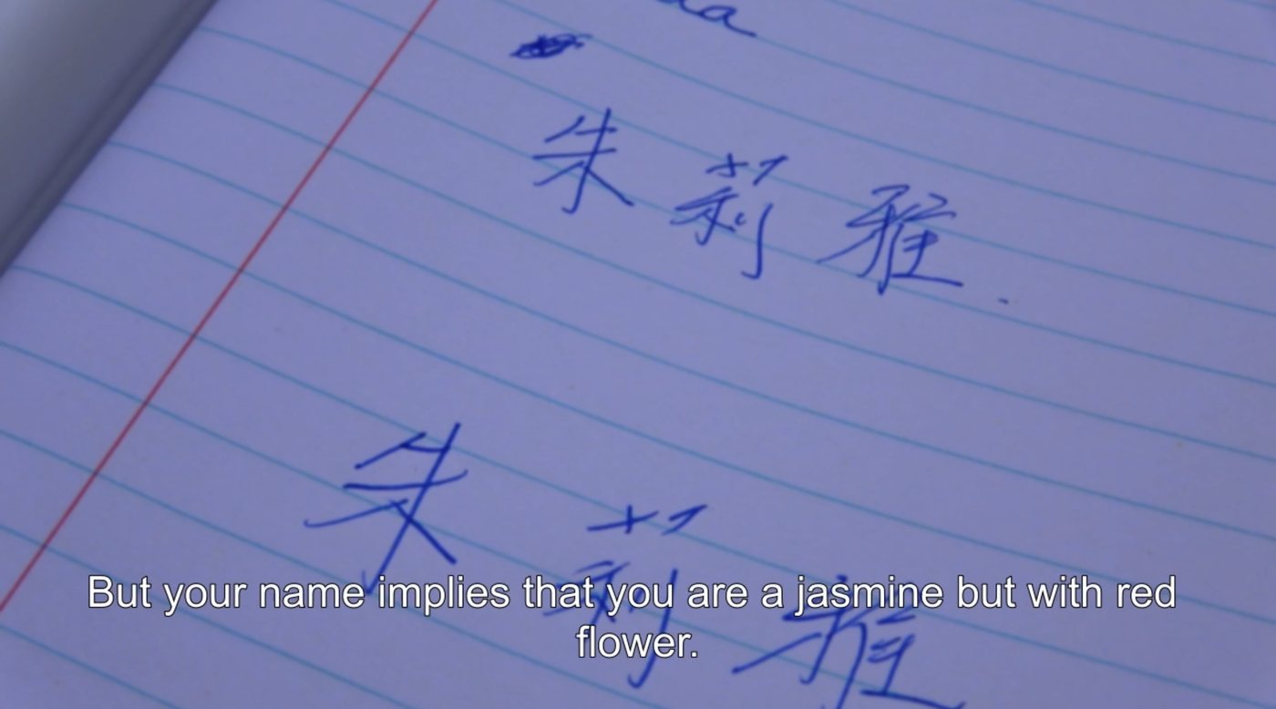 Film still: handwritten Chinese characters on lined paper; subtitle reads “But your name implies that you are a jasmine but with red flower.”