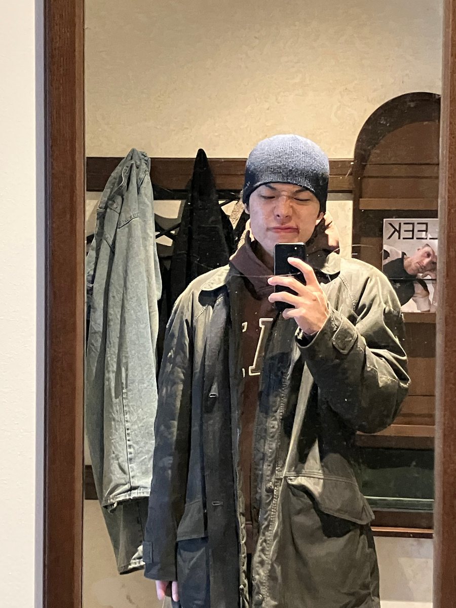 Portrait of Jie Lin in a beanie and an olive jacket, photographed in a mirror